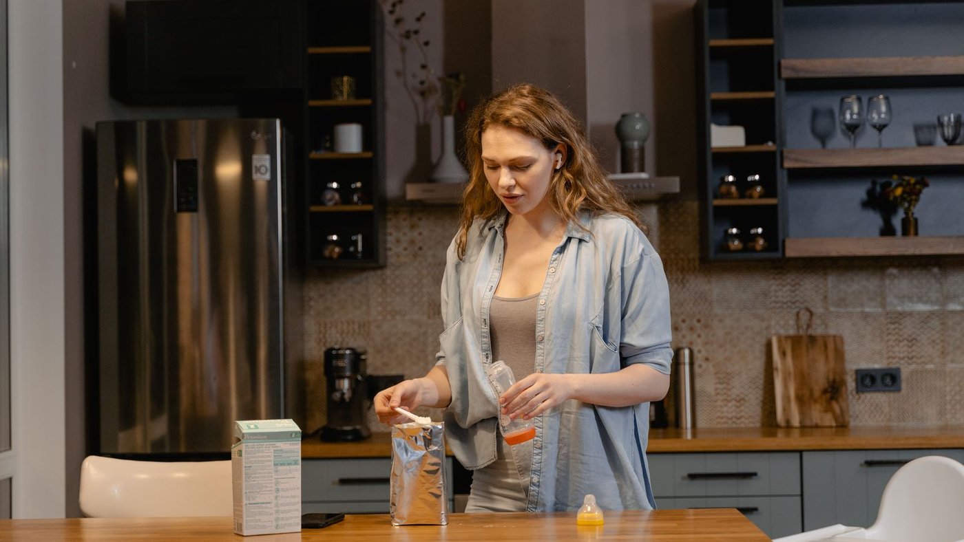A parent preparing a baby bottle in a kitchen